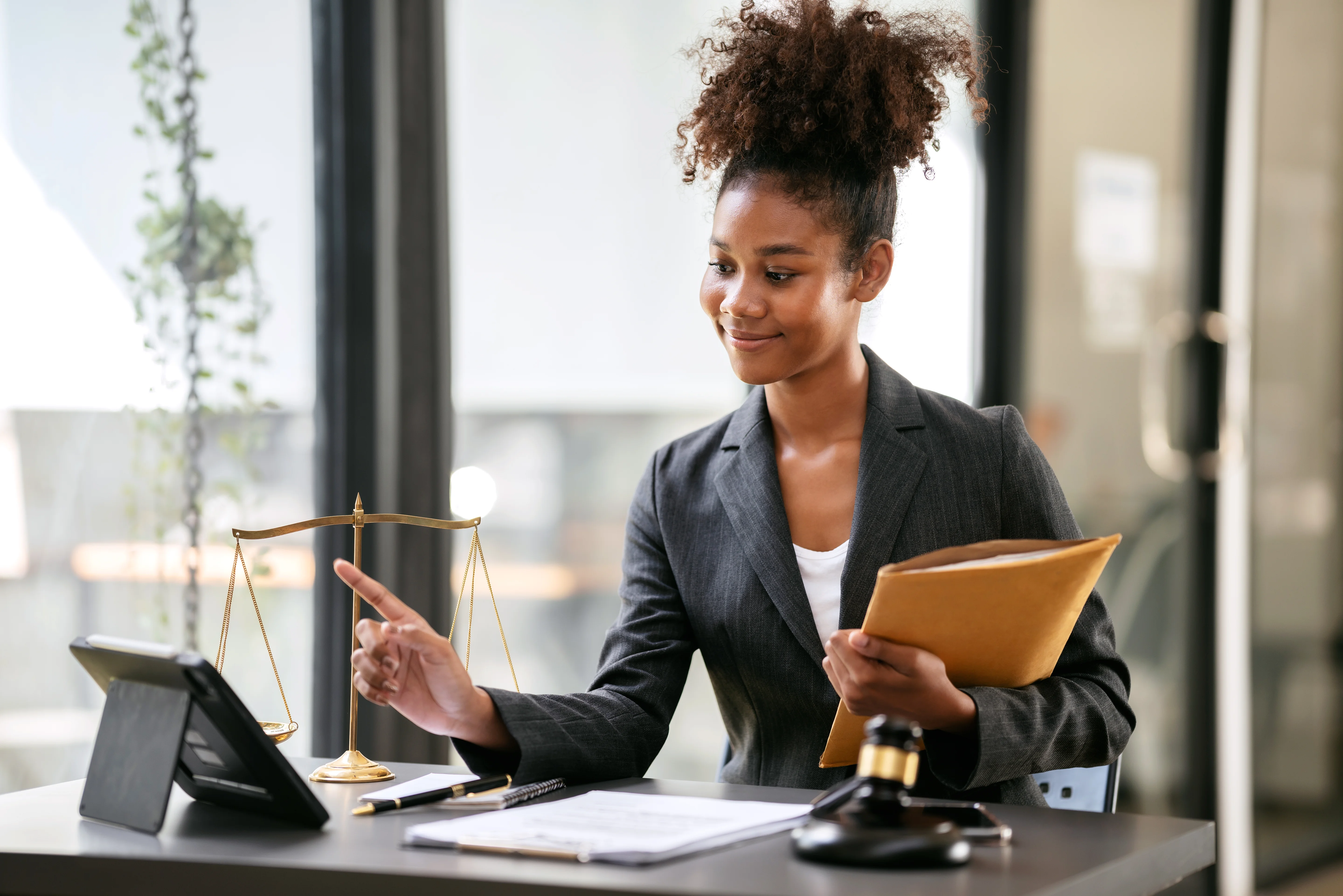 A lawyer in a suit holding an envelope of business contracts and reading information on a tablet while sitting.