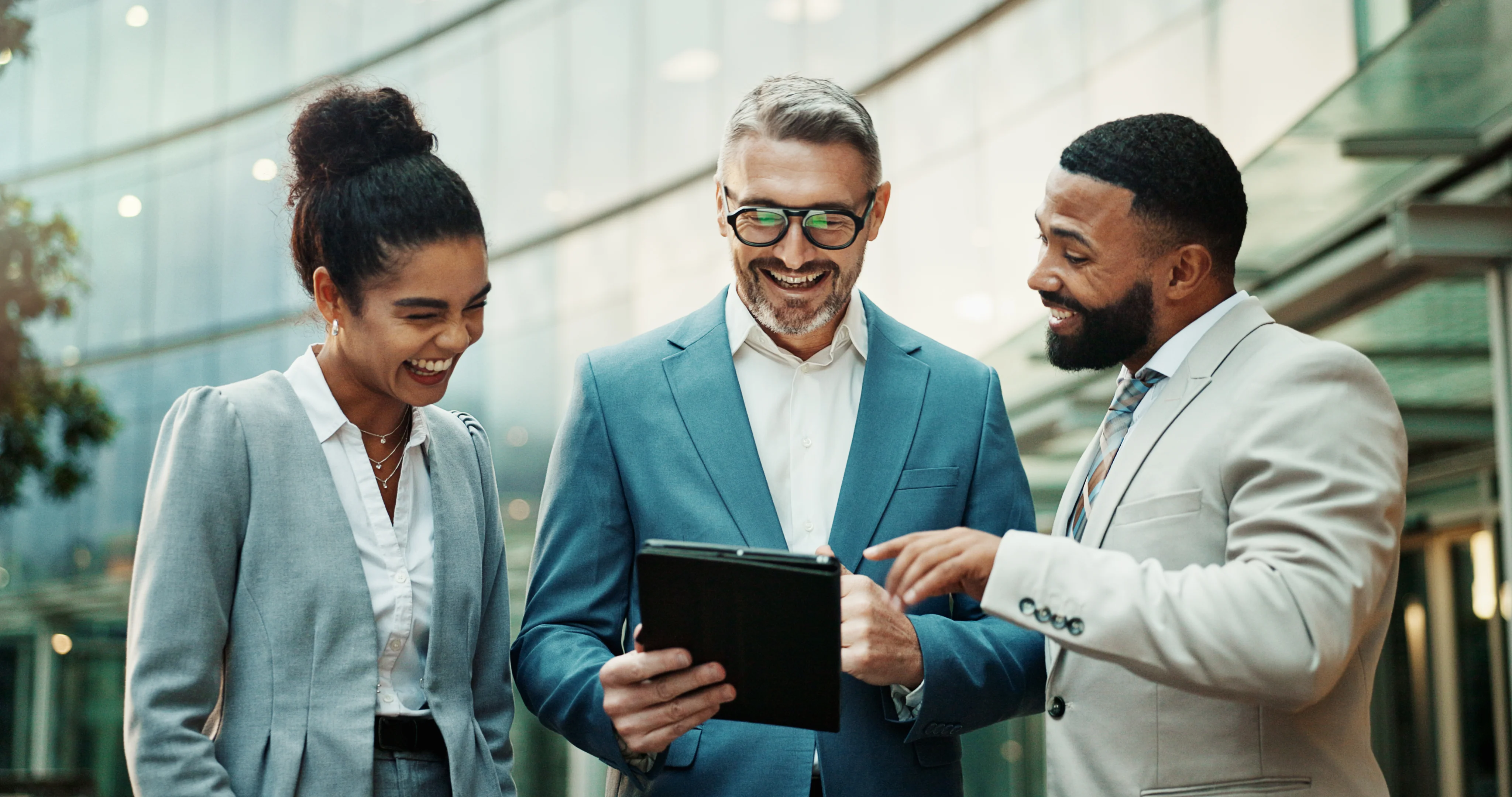 Business people in a city outdoors, smiling, standing around a tablet.