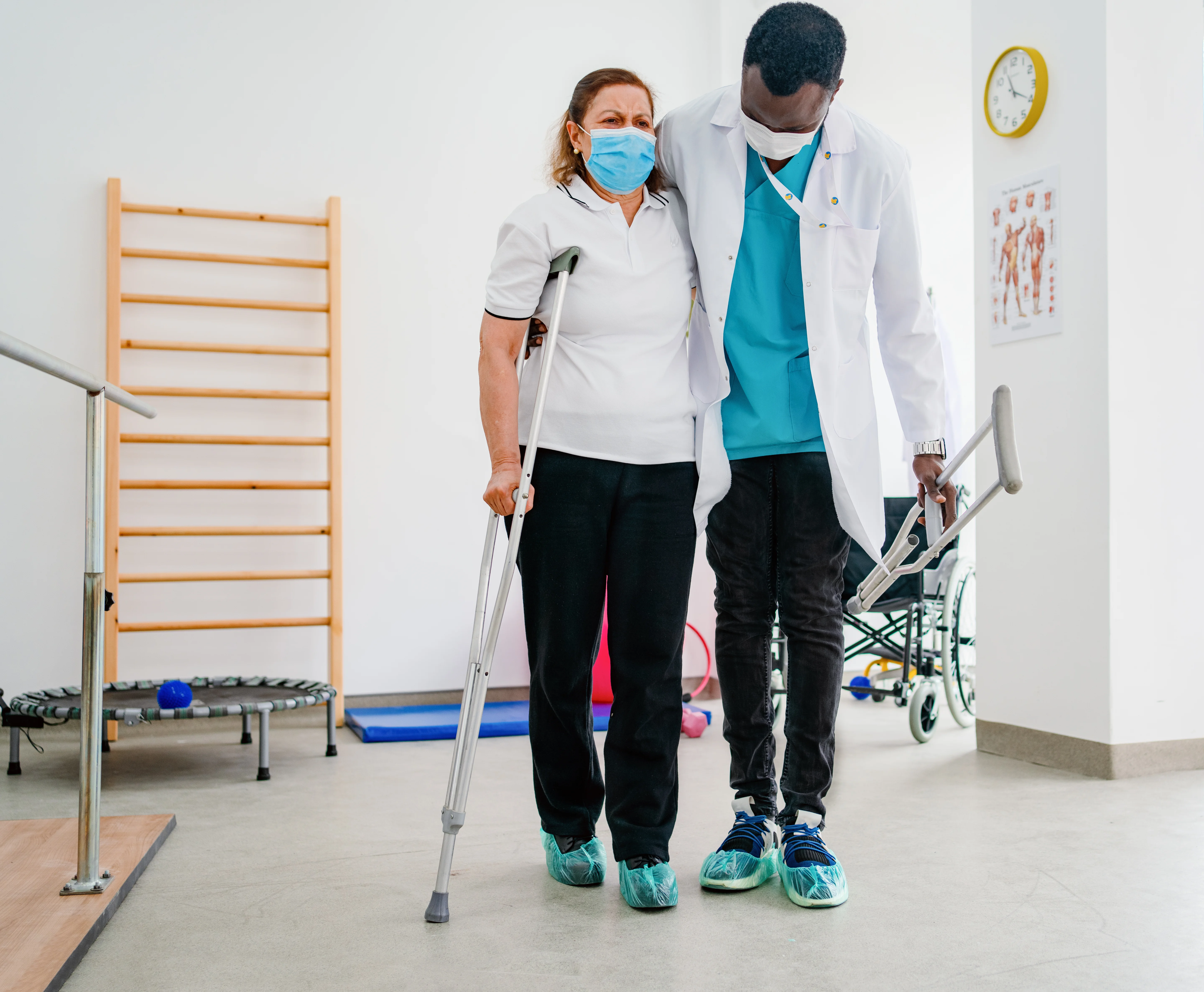Woman walking with a crutch in physiotherapy and therapist next to her helping